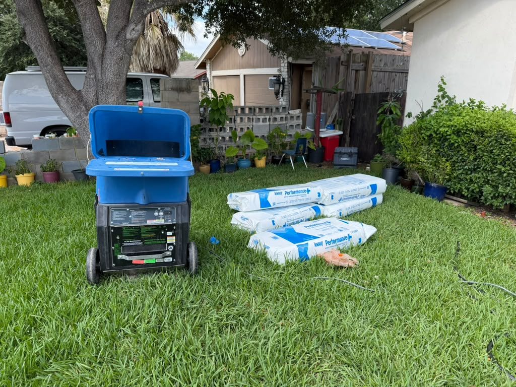 Insulation blower machine with bags of blown-in fiberglass on the lawn outside a home